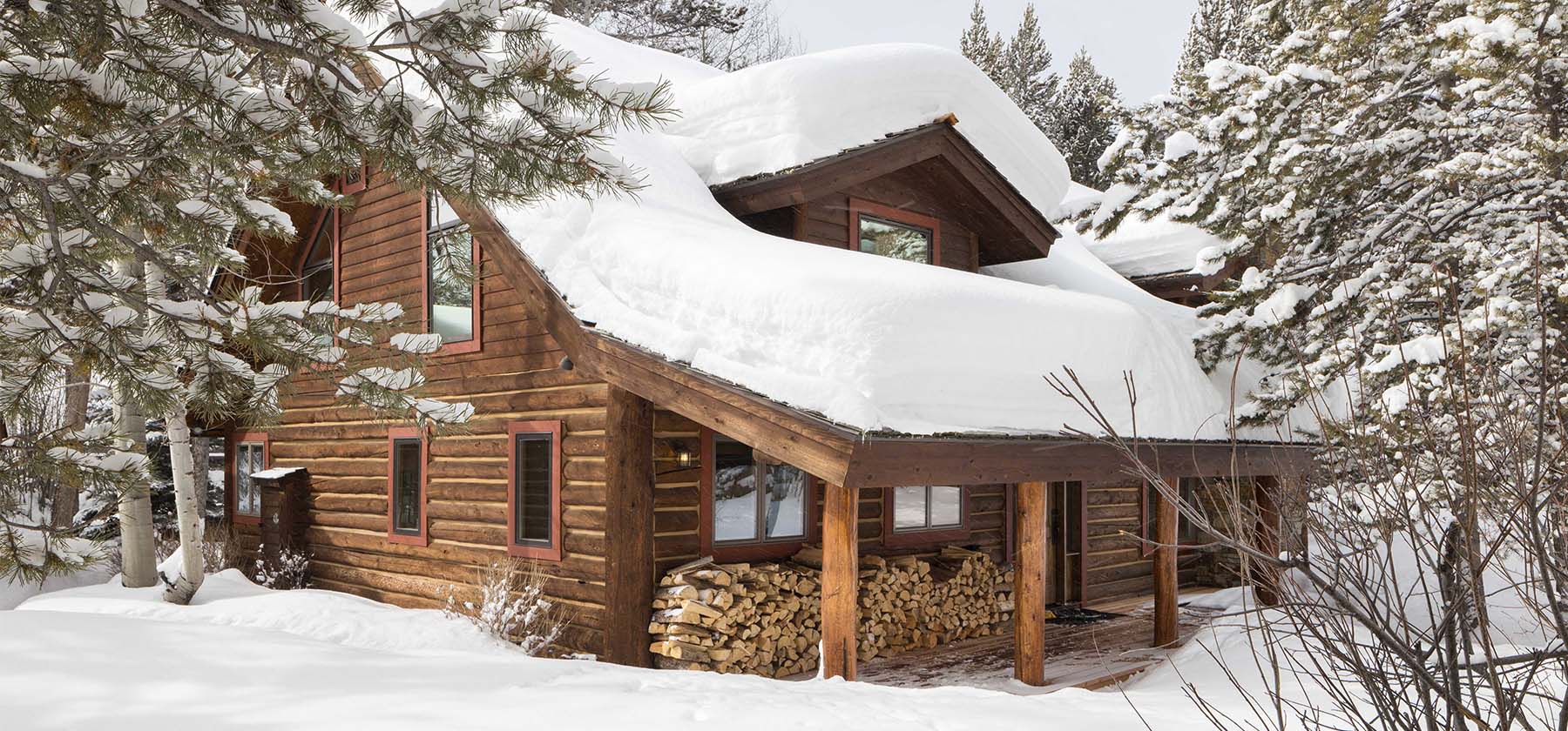 Snow-covered log cabin vacation rental surrounded by pine trees in Jackson Hole, Wyoming